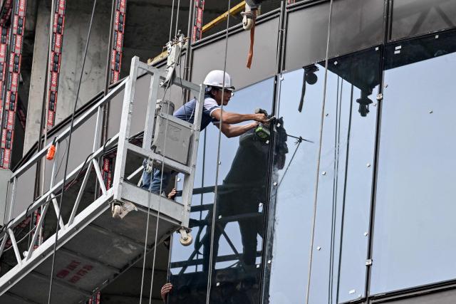 A worker installes a pane of glass at a hotel construction site in Hanoi on July 10, 2026. (Photo by Nhac NGUYEN / AFP)