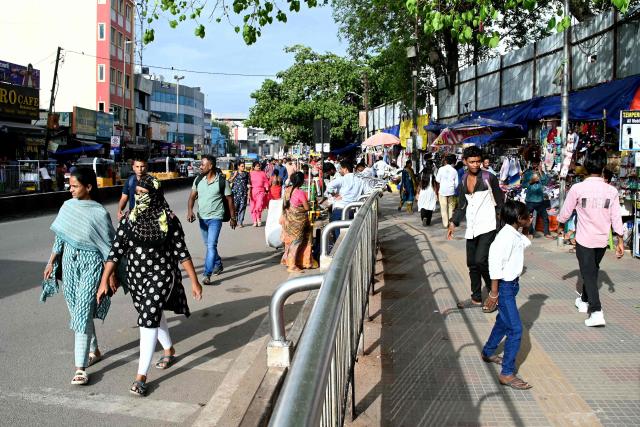 This photograph taken on July 6, 2026 shows pedestrians walking alongside a footpath on a road in Hyderabad. In India, a pavement can be many things -- hawking site, parking area, garbage dumping space -- but rarely what it is meant to be: a safe unobstructed path to walk on. (Photo by Noah SEELAM / AFP)