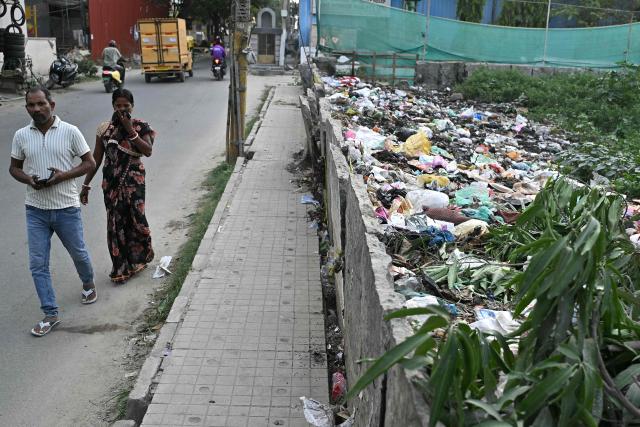 This photograph taken on July 6, 2026 shows pedestrians walking near a garbage-strewn footpath along a road in Bengaluru. In India, a pavement can be many things -- hawking site, parking area, garbage dumping space -- but rarely what it is meant to be: a safe unobstructed path to walk on. (Photo by Idrees MOHAMMED / AFP)