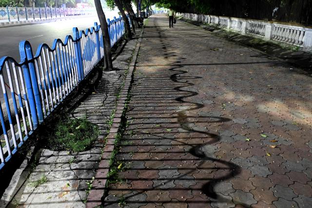 This photograph taken on July 6, 2026 shows a pedestrian walking on a footpath along a road in Kolkata. In India, a pavement can be many things -- hawking site, parking area, garbage dumping space -- but rarely what it is meant to be: a safe unobstructed path to walk on. (Photo by Dibyangshu SARKAR / AFP)