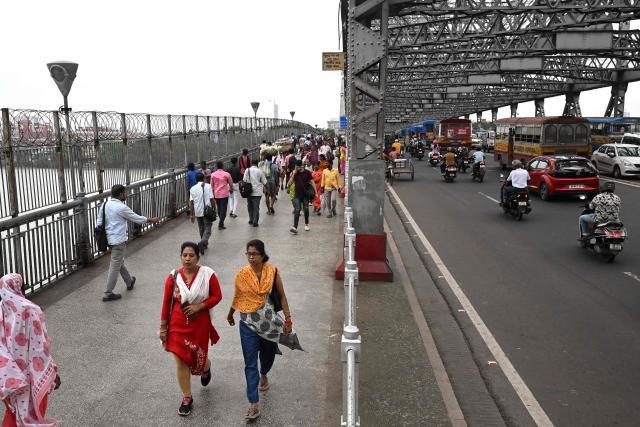 This photograph taken on July 7, 2026 shows pedestrians walking on a footpath along the Howrah Bridge in Kolkata. In India, a pavement can be many things -- hawking site, parking area, garbage dumping space -- but rarely what it is meant to be: a safe unobstructed path to walk on. (Photo by Dibyangshu SARKAR / AFP)