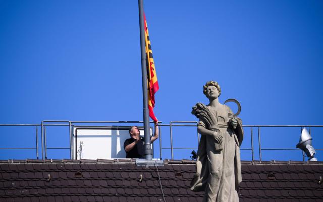 A man lowers the flag on the roof of the German President's official residence, the Bellevue Palace, as the standard is taken down to be raised again at the President's temporary residence, on July 10, 2026 in Berlin. The Bellevue Palace will undergo extensive renovation. For up to eight years, the Federal President’s Office will move to an interim residence, the "Amtssitz am Spreebogen". (Photo by Bernd von Jutrczenka / POOL / AFP)