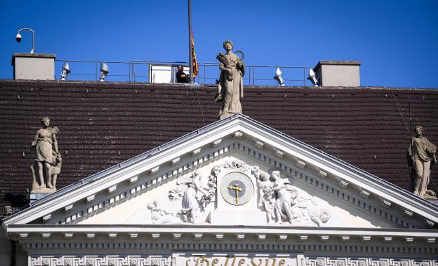 A man lowers the flag on the roof of the German President's official residence, the Bellevue Palace, as the standard is taken down to be raised again at the President's temporary residence, on July 10, 2026 in Berlin. The Bellevue Palace will undergo extensive renovation. For up to eight years, the Federal President’s Office will move to an interim residence, the "Amtssitz am Spreebogen". (Photo by Bernd von Jutrczenka / POOL / AFP)