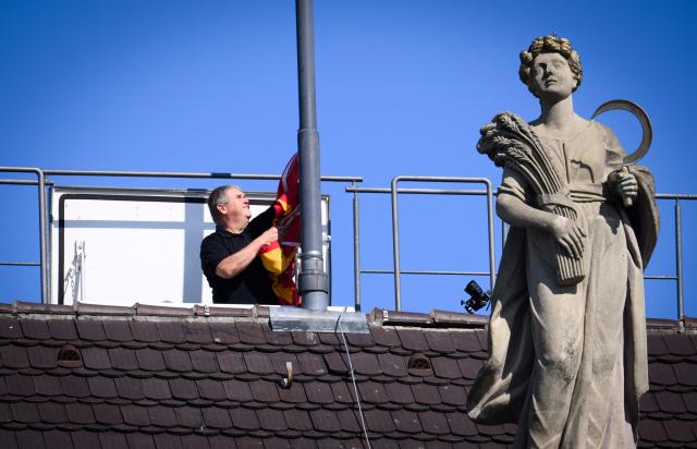 A man lowers the flag on the roof of the German President's official residence, the Bellevue Palace, as the standard is taken down to be raised again at the President's temporary residence, on July 10, 2026 in Berlin. The Bellevue Palace will undergo extensive renovation. For up to eight years, the Federal President’s Office will move to an interim residence, the "Amtssitz am Spreebogen". (Photo by Bernd von Jutrczenka / POOL / AFP)