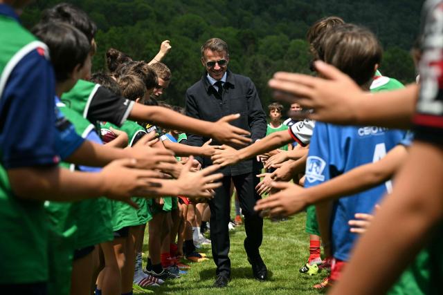 France's President Emmanuel Macron (C) checks hands with children as he visits sports facilities in Loudenvielle, south-western France, on July 10, 2026. (Photo by Lionel BONAVENTURE / POOL / AFP)