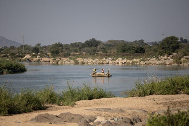 People travel aboard a makeshift boat across the Limpopo River along the South Africa-Zimbabwe border near the Beitbridge border crossing on July 9, 2026, while crossing the border outside the official port of entry. Several thousands more foreign nationals clamoured to leave South Africa on July 3, many of them gathered near the Zimbabwe border after a push that has already seen around 35,000 go home. The exodus began weeks ago as fringe groups began demanding all illegal migrants leave by June 30, in a campaign that saw violent protests and clashes. Thousands of foreigners awaited the journey home inside sprawling white tarpaulin tents serving as a temporary repatriation centre after fleeing deadly anti-immigrant protests in South Africa. More than 21,000 people had been housed and processed at the facility, according to its manager, Limpopo provincial Home Affairs chief Albert Matsaung. (Photo by EMMANUEL CROSET / AFP)