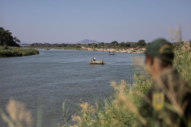 TOPSHOT - A Border Management Authority (BMA) officer watches makeshift boats cross the Limpopo River near the Beitbridge border crossing on July 9, 2026. Several thousands more foreign nationals clamoured to leave South Africa on July 3, many of them gathered near the Zimbabwe border after a push that has already seen around 35,000 go home. The exodus began weeks ago as fringe groups began demanding all illegal migrants leave by June 30, in a campaign that saw violent protests and clashes. Thousands of foreigners awaited the journey home inside sprawling white tarpaulin tents serving as a temporary repatriation centre after fleeing deadly anti-immigrant protests in South Africa. More than 21,000 people had been housed and processed at the facility, according to its manager, Limpopo provincial Home Affairs chief Albert Matsaung. (Photo by EMMANUEL CROSET / AFP)