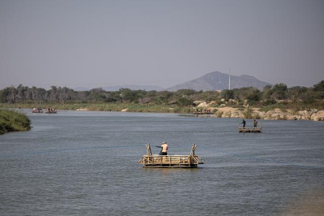 People travel aboard makeshift boats across the Limpopo River along the South Africa-Zimbabwe border near the Beitbridge border crossing on July 9, 2026, while crossing the border outside the official port of entry. Several thousands more foreign nationals clamoured to leave South Africa on July 3, many of them gathered near the Zimbabwe border after a push that has already seen around 35,000 go home. The exodus began weeks ago as fringe groups began demanding all illegal migrants leave by June 30, in a campaign that saw violent protests and clashes. Thousands of foreigners awaited the journey home inside sprawling white tarpaulin tents serving as a temporary repatriation centre after fleeing deadly anti-immigrant protests in South Africa. More than 21,000 people had been housed and processed at the facility, according to its manager, Limpopo provincial Home Affairs chief Albert Matsaung. (Photo by EMMANUEL CROSET / AFP)