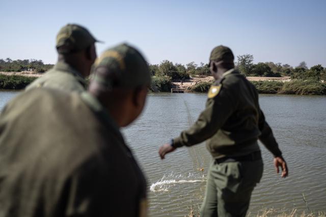 Border Management Authority (BMA) officers cut a cable used to pull makeshift boats across the Limpopo River near the Beitbridge border crossing on July 9, 2026. Several thousands more foreign nationals clamoured to leave South Africa on July 3, many of them gathered near the Zimbabwe border after a push that has already seen around 35,000 go home. The exodus began weeks ago as fringe groups began demanding all illegal migrants leave by June 30, in a campaign that saw violent protests and clashes. Thousands of foreigners awaited the journey home inside sprawling white tarpaulin tents serving as a temporary repatriation centre after fleeing deadly anti-immigrant protests in South Africa. More than 21,000 people had been housed and processed at the facility, according to its manager, Limpopo provincial Home Affairs chief Albert Matsaung. (Photo by EMMANUEL CROSET / AFP)