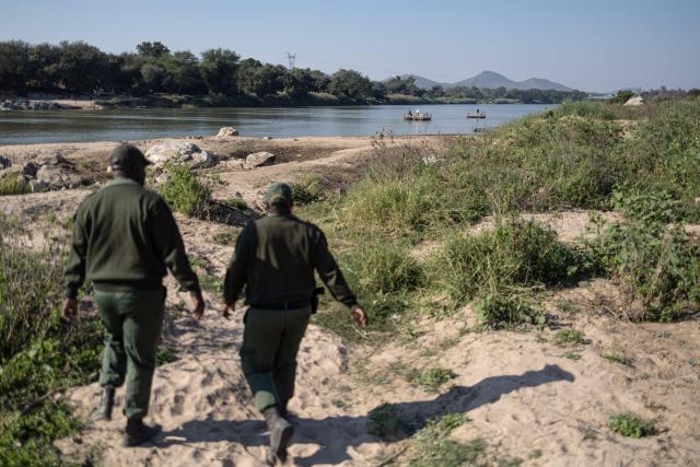 Border Management Authority (BMA) officers walk toward makeshift boats crossing the Limpopo River near the Beitbridge border crossing on July 9, 2026. Several thousands more foreign nationals clamoured to leave South Africa on July 3, many of them gathered near the Zimbabwe border after a push that has already seen around 35,000 go home. The exodus began weeks ago as fringe groups began demanding all illegal migrants leave by June 30, in a campaign that saw violent protests and clashes. Thousands of foreigners awaited the journey home inside sprawling white tarpaulin tents serving as a temporary repatriation centre after fleeing deadly anti-immigrant protests in South Africa. More than 21,000 people had been housed and processed at the facility, according to its manager, Limpopo provincial Home Affairs chief Albert Matsaung. (Photo by EMMANUEL CROSET / AFP)