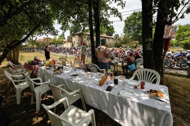 The pack of riders (peloton) cycles past spectators by a long picnic table along the roadside at the start of the 7th stage of the 113th edition of the Tour de France cycling race, 175 km between Hagetmau and Bordeaux in southwestern France, on July 10, 2026. (Photo by Anne-Christine POUJOULAT / AFP)
