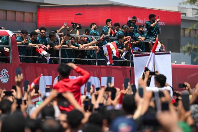 Egyptian fans cheer on Egypt's players as they ride atop an open-top bus after they have arrived at El-Alamein International Airport in the northern coastal city of El-Alamein on July 10, 2026, following their participation in the 2026 World Cup football tournament. Hundreds of euphoric supporters welcomed home Egypt's national football team in the coastal city of El-Alamein on July 10 after a historic World Cup campaign that ended with a thrilling last-16 defeat to Argentina. (Photo by AFP)