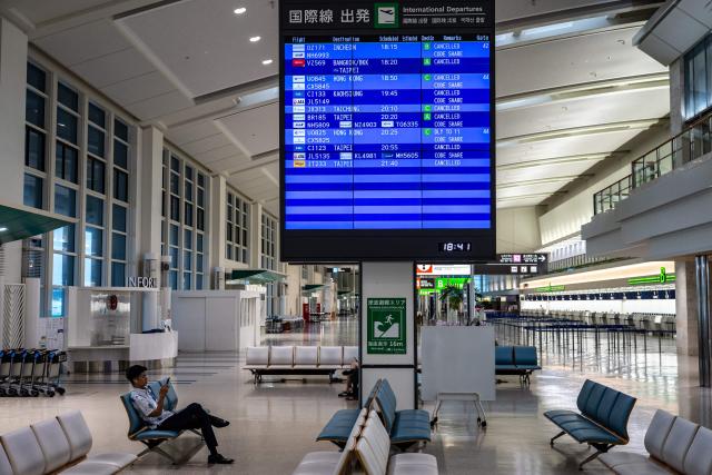 A man sits next to a screen showing cancelled flights at the departure hall at Naha Airport in Naha, Okinawa prefecture, on July 10, 2026. Typhoon Bavi is expected to pound Taiwan's north and east, as well as Japan's remote southwestern islands, on July 10 and 11 before smashing into China, which has been hit by deadly storms this week. (Photo by Philip FONG / AFP)