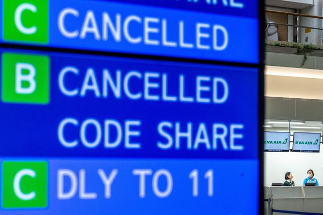 A screen showing cancelled flights is seen as staff members stand by at a check-in counter at Naha Airport in Naha, Okinawa prefecture, on July 10, 2026. Typhoon Bavi is expected to pound Taiwan's north and east, as well as Japan's remote southwestern islands, on July 10 and 11 before smashing into China, which has been hit by deadly storms this week. (Photo by Philip FONG / AFP)