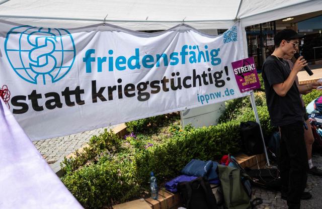 An activist addresses demonstrators in front of the German Red Cross (DRK) hospital in Berlin's Wedding district, on July 10, 2026, during a protest against an alleged militarisation of the German healthcare system. The banner reads: "Peace-loving rather than war-mongering". (Photo by John MACDOUGALL / AFP)