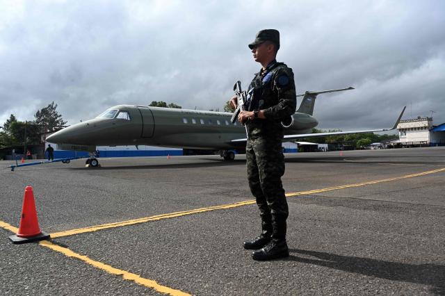A soldier stands guard by the Honduran presidential airplane, which will be auctioned off as part of austerity measures, as it remains parked at the Hernan Acosta Mejia Air Base in Tegucigalpa on July 10, 2026. The Embraer Legacy 600 jet, which purchase and maintenance have been marred by allegations of corruption, was acquired by Honduran President (2014–2022) Juan Orlando Hernandez. (Photo by Orlando SIERRA / AFP)
