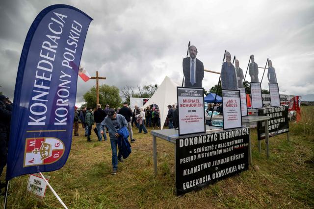 Banners reading 'I do not apologise for Jedwabne – let the perpetrators apologise' and 'Finish the exhumation – put an end to the slanders against Poles – the Jedwabne lie', with cut-out figures depicting Poland's Chief Rabbi Michael Schudrich and former Polish presidents are displayed near a crucifix set up at a gathering of far-right supporters who question the guilt of Polish citizens for the massacre in Jedwabne, on the sidelines of an official ceremony at the Jedwabne massacre monument honouring the memory of the town's Jewish residents murdered on July 10, 1941 by their Polish neighbours, in Jedwabne, north-eastern Poland, on July 10, 2026. Poland's Jewish community, political leaders and ordinary citizens on July 10 commemorated a massacre of hundreds of Jews killed by their Polish neighbors 85 years ago in the town of Jedwabne in then German-occupied Poland, at a ceremony opposed by far-right demonstrators. (Photo by Wojtek RADWANSKI / AFP)