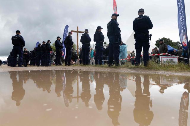 Police officers are reflected in a puddle as they stand guard during a gathering of far-right supporters, who question the guilt of the Polish citizens responsible for the Jedwabne massacre and place all the blame on the German pacification unit, on the sidelines of the official ceremonies at the Jedwabne massacre monument honouring the memory of the town's Jewish residents murdered on July 10, 1941 by their Polish neighbours, in Jedwabne, north-eastern Poland, on July 10, 2026. Poland's Jewish community, political leaders and ordinary citizens on July 10 commemorated a massacre of hundreds of Jews killed by their Polish neighbors 85 years ago in the town of Jedwabne in then German-occupied Poland, at a ceremony opposed by far-right demonstrators. (Photo by Wojtek RADWANSKI / AFP)