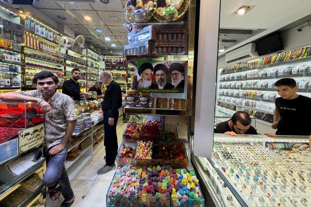 A poster bearing the portraits of Iran's late supreme leader Ayatollah Ruhollah Khomeini (L), Iran's supreme leader Mojtaba Khamenei (C) and slain supreme leader Ali Khamenei hangs at a shop at the Grand Reza Bazaar near the shrine of Imam Reza following the funeral of slain Iranian leader Ali Khamenei and his family members in Mashhad on July 10, 2026. Iran on July 10 laid to rest its former supreme leader Ali Khamenei over four months after his killing in an airstrike, as two days of US and Iranian attacks raised fears of a return to all-out war. (Photo by ATTA KENARE / AFP) / 