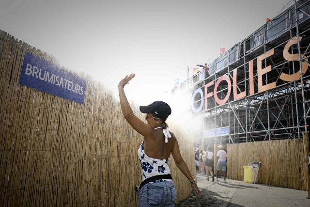A woman cools off under a water mist diffuser as festivalgoers arrive on the opening day of the 42nd Francofolies music festival in La Rochelle, western France, on July 10, 2026, as a heatwave hits France. (Photo by Philippe LOPEZ / AFP)