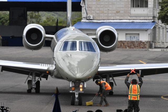 Workers are seen next to the Honduran presidential airplane after it was auctioned off as part of austerity measures, at the Hernan Acosta Mejia Air Base in Tegucigalpa on July 10, 2026. The Embraer Legacy 600 jet, which purchase and maintenance have been marred by allegations of corruption, was acquired by former Honduran President (2014–2022) Juan Orlando Hernandez. It was purchased on July 10, 2026 by THEBE, an engineering and consultancy firm based in Mexico. (Photo by Orlando SIERRA / AFP)