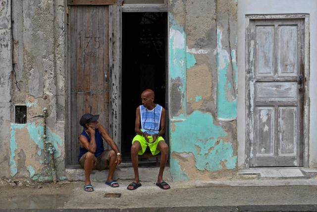 Two men sit at the doorstep to avoid the heat during a nationwide power outage on July 10, 2026. Cuba suffered its second nationwide blackout in five days on July 10 as twin energy and economic crises, compounded by a six-month US fuel blockade, caused the electricity grid to collapse. (Photo by YAMIL LAGE / AFP)