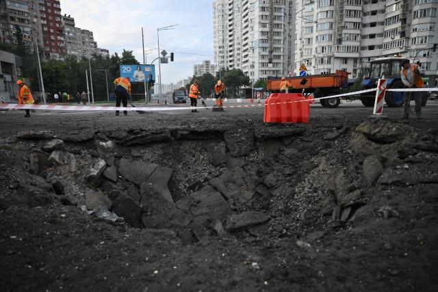 Communal workers clean around a crater from Russian missile strikes on the Ukrainian capital of Kyiv early on July 11, 2026, amid the Russian invasion in Ukraine. Ukraine said Russian missile strikes on Kyiv wounded six people, as Moscow escalates attacks on the Ukrainian capital. AFP journalists in Kyiv heard two series of explosions in the early hours of Saturday, with an air alert siren sounding minutes after the first blast. (Photo by Genya Savilov / AFP)