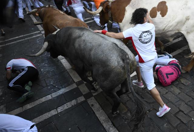 Participants fall as they run ahead of bulls through the Mercaderes curve during the fifth running of the bulls of the San Fermin festival in Pamplona, northern Spain, on July 11, 2026. Thousands of people every year attend the week-long festival and its famous 'encierros', or running of the bulls, in which six bulls are released at 8:00 a.m. evey day to run from their corral to the bullring through the narrow streets of the old town over an 850 meters (yards) course while runners ahead of them try to stay close to the bulls without falling over or being gored. (Photo by Miguel RIOPA / AFP)