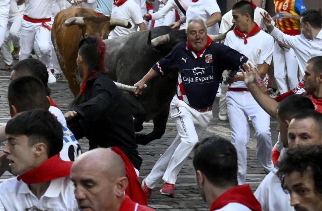 Participants fall as they run ahead of bulls through the Mercaderes curve during the fifth running of the bulls of the San Fermin festival in Pamplona, northern Spain, on July 11, 2026. Thousands of people every year attend the week-long festival and its famous 'encierros', or running of the bulls, in which six bulls are released at 8:00 a.m. evey day to run from their corral to the bullring through the narrow streets of the old town over an 850 meters (yards) course while runners ahead of them try to stay close to the bulls without falling over or being gored. (Photo by Miguel RIOPA / AFP)