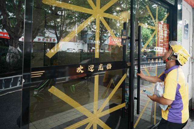 A food delivery man opens a door with taped glass at a restaurant, as people prepare from approaching Typhoon Bavi to hit the region, in Hangzhou, China's eastern province on July 11, 2026. (Photo by CN-STR / AFP) / China OUT