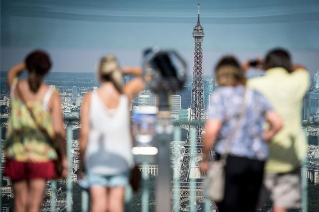 (FILES) Tourists take pictures and enjoy the panoramic view of the Eiffel Tower and the city of Paris, from the Tour Montparnasse on August 6, 2018. The Eiffel Tower will close from 4:00 PM this weekend due to the heatwave, according to the operator on July 11, 2026. (Photo by GERARD JULIEN / AFP)