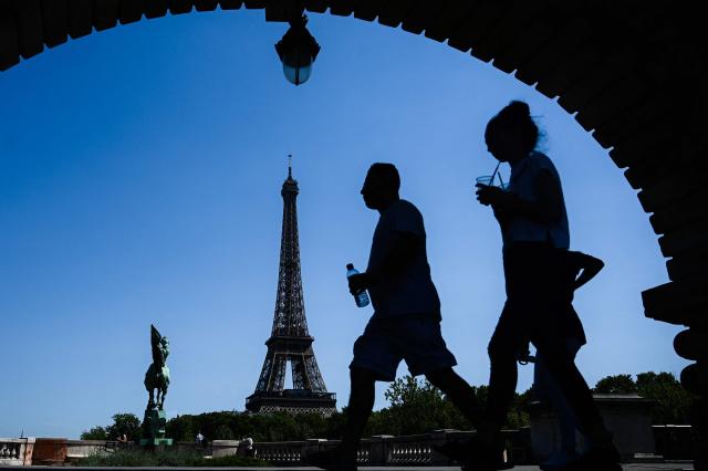 (FILES) A man holding a bottle of water walks by a woman sipping a drink through a straw on a bridge over the Seine river in front of the Eiffel Tower in Paris on July 23, 2019. The Eiffel Tower will close from 4:00 PM this weekend due to the heatwave, according to the operator on July 11, 2026. (Photo by Philippe LOPEZ / AFP)