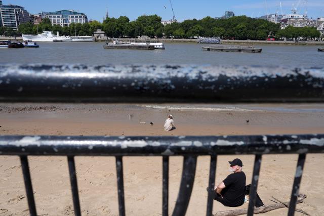 People sit on the river bed of the River Thames, in central London on July 11, 2026, as the British capital continues to experience high temperatures. Britain's Met office said on July 9, that the UK had experienced its eighth day in 2026 with the mercury climbing above 34C, breaking the previous record by one day. (Photo by CARLOS JASSO / AFP)