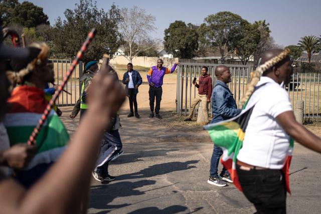 A petrol attendant on break looks on as protesters march during a anti-migration demonstration in Norwood on July 11, 2026. Protests that began with groups like March and March have since spread to ordinary residents taking to the streets, as anti-migrant sentiment continues to spread across South Africa. (Photo by EMMANUEL CROSET / AFP)