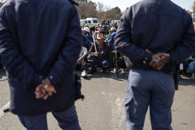Protesters gather in front a Builders hardware store as South African Police Service (SAPS) officers stand guard during an anti-migration demonstration in Norwood on July 11, 2026. Protests that began with groups like March and March have since spread to ordinary residents taking to the streets, as anti-migrant sentiment continues to spread across South Africa. (Photo by EMMANUEL CROSET / AFP)