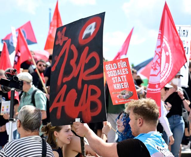 Demonstrators hold a placard (L) reading "1312 ACAB" (the abbreviation and numeric code for the slogan All Cops are Bastards) and a poster reading "Money for social welfare rather than for war" (R) during an anti-war and anti-military service demonstration organised by an action group against German arms manufacturer Rheinmetall planning to construct an ammunition plant in the Wedding district of the German capital, in Berlin, Germany, on July 11, 2026. (Photo by Tobias SCHWARZ / AFP)