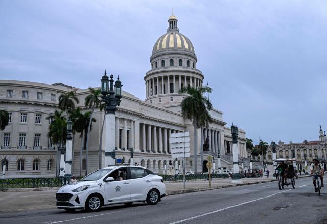 A police patrol car and cyclists pass by the Havana Capitol on July 11, 2026. Cuba suffered its second nationwide blackout in five days on July 10 as twin energy and economic crises, compounded by a six-month US fuel blockade, caused the electricity grid to collapse. (Photo by YAMIL LAGE / AFP)