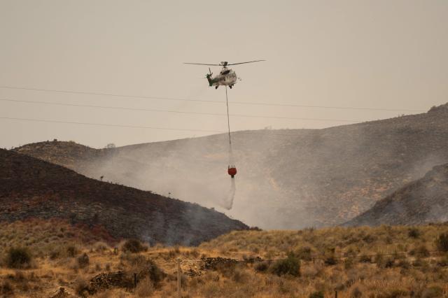 A picture taken on July 11, 2026 shows a helicopter of Infoca (Andalusia Wildfire Service) dropping water as firefighters continue to battle a wildfire that killed at least 12 people, near Los Gallardos, near Almeria on July 11, 2026. Firefighters aided by better weather on July 11 gained the upper hand on one of Spain's deadliest wildfires, that killed at least 12 people and burned about 6,600 hectares (16,300 acres) since July 9. (Photo by JORGE GUERRERO / AFP)