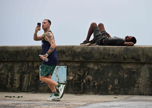 A man rests on the Malecon as another person jogs past while looking at a mobile phone in Havana on July 11, 2026. Cuba suffered its second nationwide blackout in five days on July 10 as twin energy and economic crises, compounded by a six-month US fuel blockade, caused the electricity grid to collapse. (Photo by YAMIL LAGE / AFP)