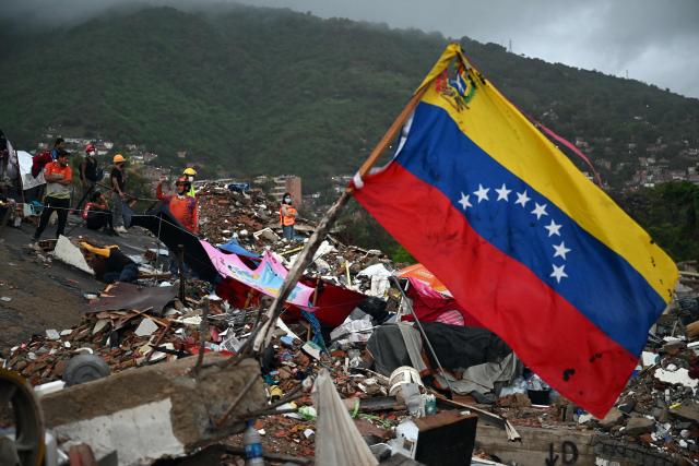 Venezuelan flag flies above the rubble as rescue workers conduct a search operation at the site of collapsed buildings in Caraballeda, La Guaira state, Venezuela, on July 11, 2026, following twin earthquakes that struck the region. The death toll from the twin earthquakes that struck Venezuela on June 24 has risen to more than 4,300, National Assembly President Jorge Rodriguez said on July 11. (Photo by Raul ARBOLEDA / AFP)