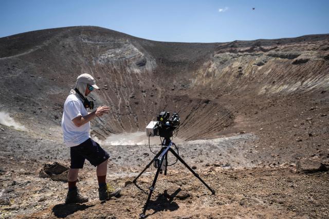 A volcanologist from the University of Munich works with a laser instrument to gather data from a drone in the crater of La Fossa on Vulcano Island, one of the seven islands Aeolian Archipelago of Sicily, on July 9, 2026. A team of researchers from Germany are testing a new system for measuring volcanic gases to better anticipate future eruptions. Hovering over the crater of La Fossa, a drone positions itself in front of a laser beam set at the edge of the chasm on Vulcano, off Sicily, and collect data. (Photo by Marco Bertorello / AFP)