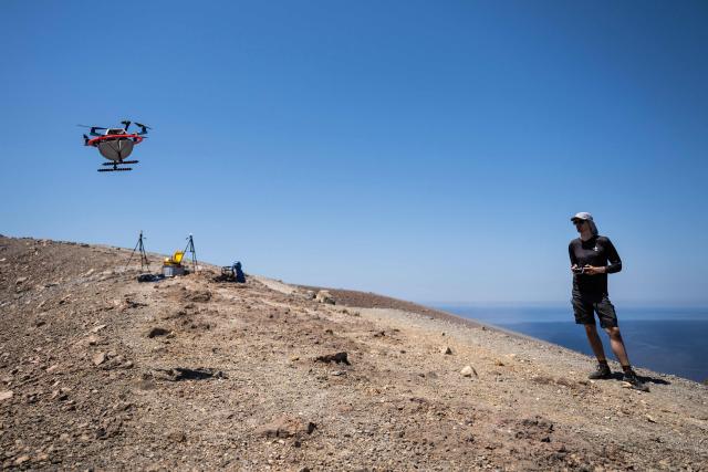 A vulcanologist from the University of Munich pilots a drone with a mirror used to reflect a laser and collect data from gas emissions in the crater of La Fossa, on Vulcano Island, one of the seven islands of the Aeolian Archipelago of Sicily, on July 9, 2026. A team of researchers from Germany are testing a new system for measuring volcanic gases to better anticipate future eruptions. Hovering over the crater of La Fossa, a drone positions itself in front of a laser beam set at the edge of the chasm on Vulcano, off Sicily, and collect data. (Photo by Marco Bertorello / AFP)