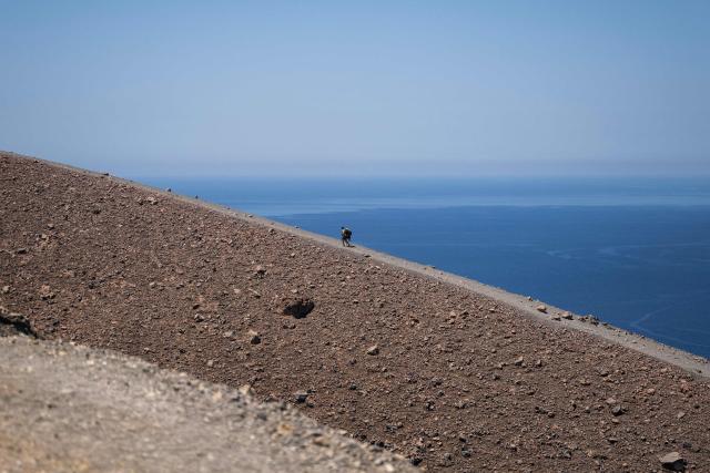 People walk on the edge of the crater of La Fossa, on Vulcano Island, in the Aeolian Archipelago of Sicily, on 9 July 2026. A team of researchers from Germany are testing a new system for measuring volcanic gases to better anticipate future eruptions. Hovering over the crater of La Fossa, a drone positions itself in front of a laser beam set at the edge of the chasm on Vulcano, off Sicily, and collect data. (Photo by Marco Bertorello / AFP)