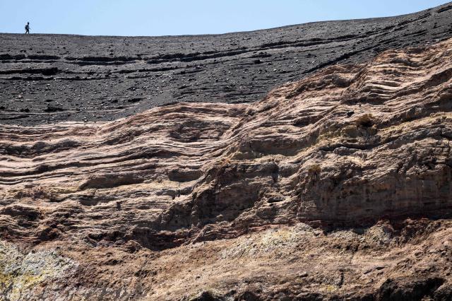People walk on the edge of the crater of La Fossa, on Vulcano Island, in the Aeolian Archipelago of Sicily, on 9 July 2026. A team of researchers from Germany are testing a new system for measuring volcanic gases to better anticipate future eruptions. Hovering over the crater of La Fossa, a drone positions itself in front of a laser beam set at the edge of the chasm on Vulcano, off Sicily, and collect data. (Photo by Marco Bertorello / AFP)