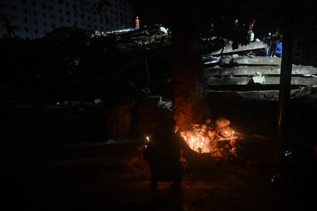 A person lights a candle as rescue workers search through the rubble of the collapsed Obras del Poder Popular (OPP) building in Caraballeda, La Guaira state, Venezuela, on July 11, 2026, following twin earthquakes that struck the region. The death toll from the twin earthquakes that struck Venezuela on June 24 has risen to more than 4,300, National Assembly President Jorge Rodriguez said on July 11. (Photo by Juan BARRETO / AFP)