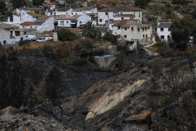 A burnt landscape is seen in front of houses following a wildfire that killed at least 12 people, in Almocaizar, Almeria Province, where authorities are investigating the origin of the fire, on July 12, 2026. A wildfire that has killed at least 12 people in southern Spain was close to being brought under control Sunday, allowing hundreds of evacuated residents to return home as firefighters worked to fully stabilise the blaze, offficials said. Authorities have kept the death toll at 12 and cautioned that the number of missing people remains uncertain until autopsies and the identification of recovered bodies are completed. (Photo by JOSE JORDAN / AFP)