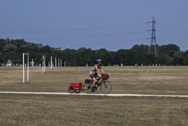 A cyclist rides past football goals (L), on pitches with dried and yellowed grass, following three heatwaves so far this summer, at Hackney Marshes in north-east London on July 12, 2026. (Photo by JUSTIN TALLIS / AFP)