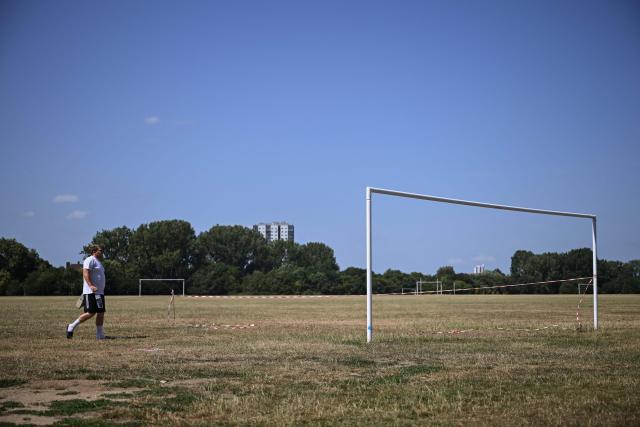 A man walks past a closed-off football goal, on a pitch with dried and yellowed grass following three heatwaves so far this summer, at Hackney Marshes in north-east London on July 12, 2026. (Photo by JUSTIN TALLIS / AFP)