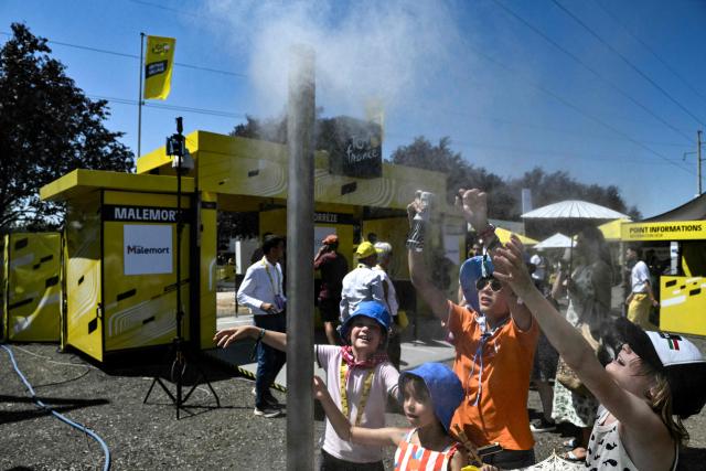 TOPSHOT - Children reach out at a mist dispenser at the start of the 9th stage of the 113th edition of the Tour de France cycling race, 154,6 km between Malemort and Ussel in central France, on July 12, 2026. (Photo by Jeff PACHOUD / AFP)