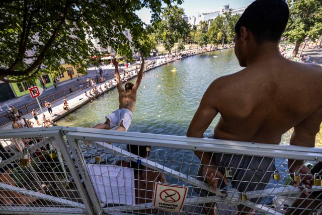A man jumps from a bridge into the Canal Saint-Martin, next to a sign prohibiting diving, as France experiences a heatwave, in Paris on July 12, 2026. (Photo by Behrouz MEHRI / AFP)